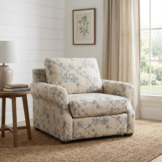 Floral armchair by window, side table with lamp and books, art on wall.