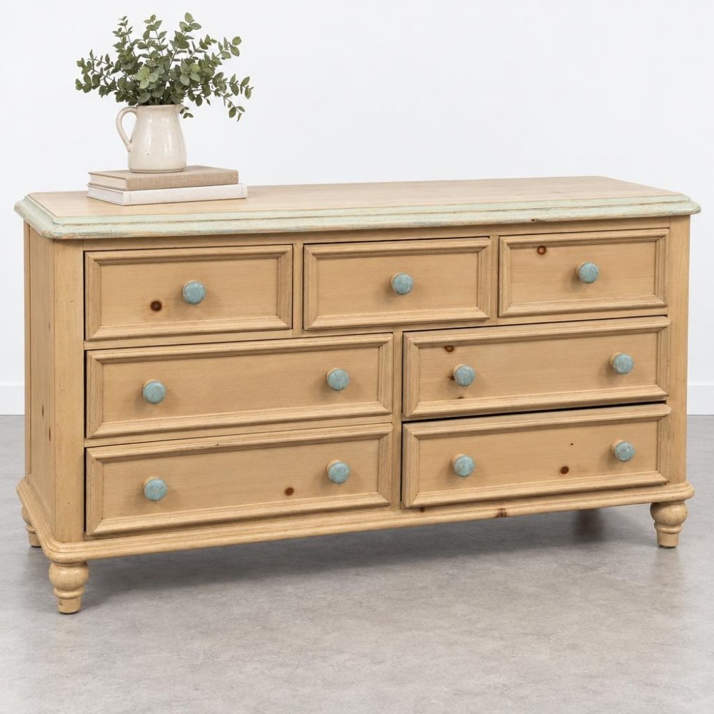 A rustic wooden dresser with turquoise knobs, topped with books and a vase of greenery.