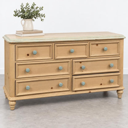 A rustic wooden dresser with turquoise knobs, topped with books and a vase of greenery.