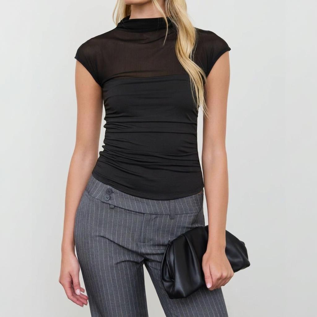 Woman in black top and pinstripe pants holding a black clutch.