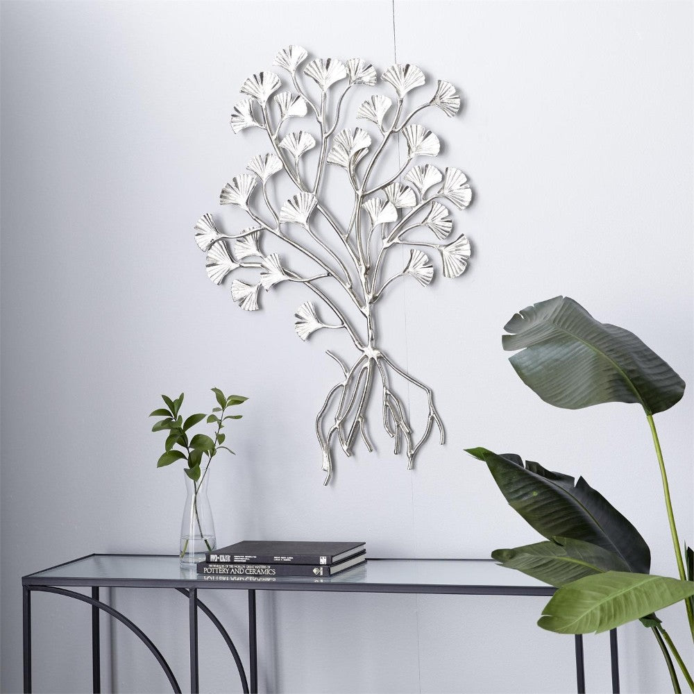 Silver tree wall art with plants and books on a glass table.
