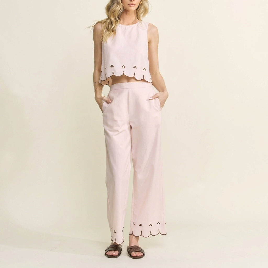 Woman in a pink scalloped top and pants, hands in pockets.