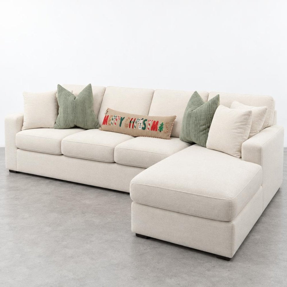 Cream sectional sofa with chaise, festive holiday pillow, and green cushions.