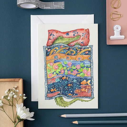 Illustrated crocodile in bed with vibrant patterned blankets.