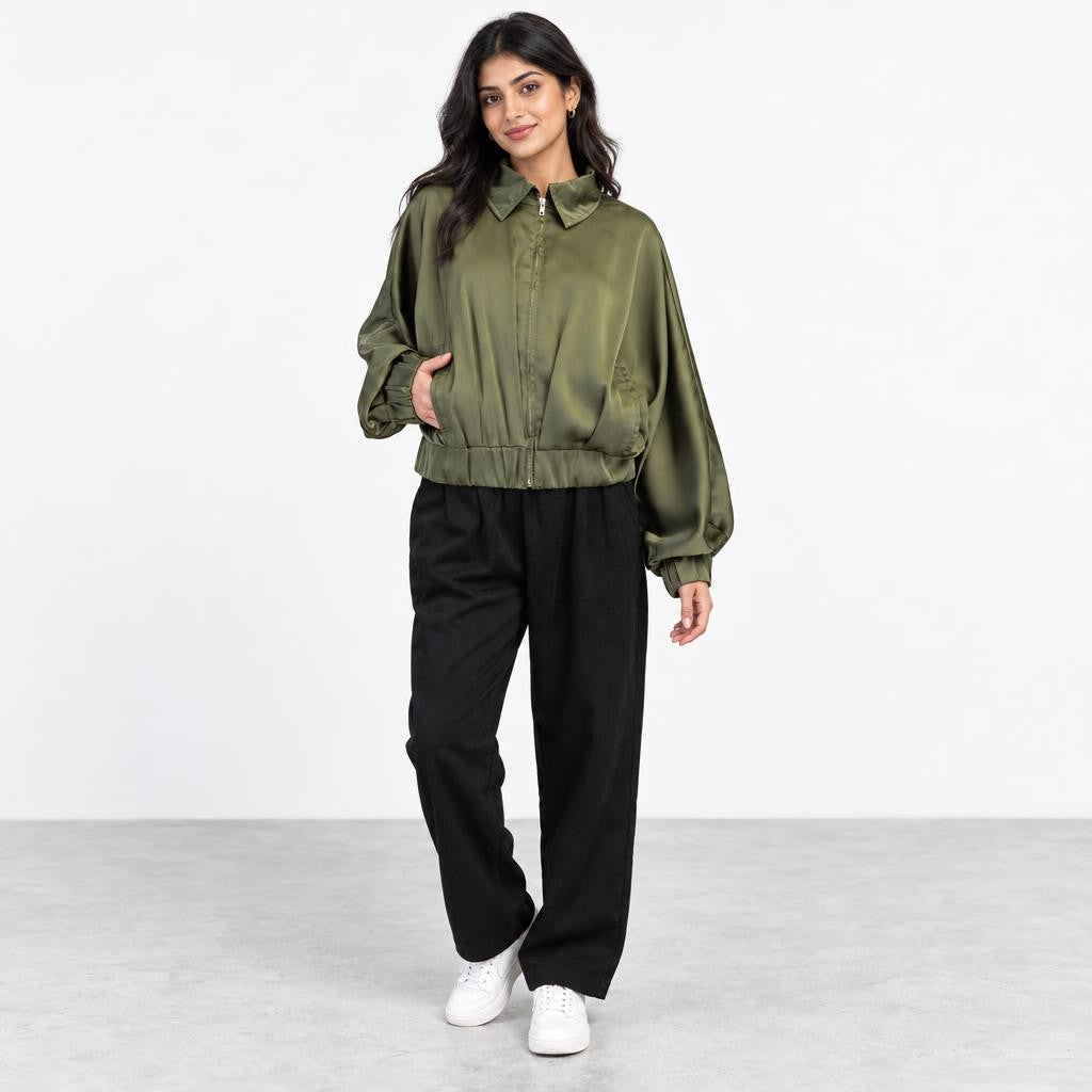 A woman models an olive green jacket, black trousers, and white sneakers against a plain backdrop.