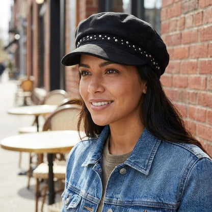 Person in a cap and denim jacket smiling outdoors by a brick wall.