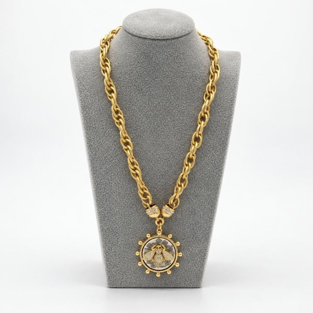 Gold chain necklace with an ornate circular pendant displayed on a gray jewelry bust.