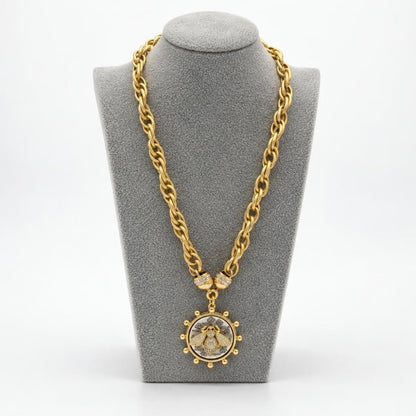 Gold chain necklace with an ornate circular pendant displayed on a gray jewelry bust.