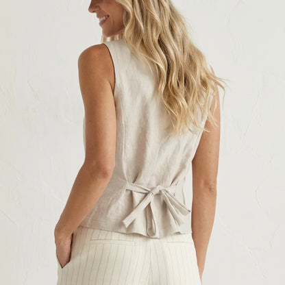 Woman in light outfit with tied-back top and striped pants, smiling slightly.