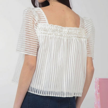 Woman wears a sheer, striped white blouse with ruffled details.