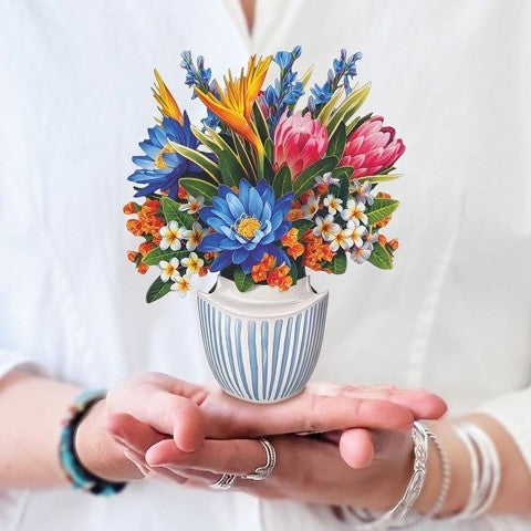 Hands holding a tiny pot with vibrant paper flowers.