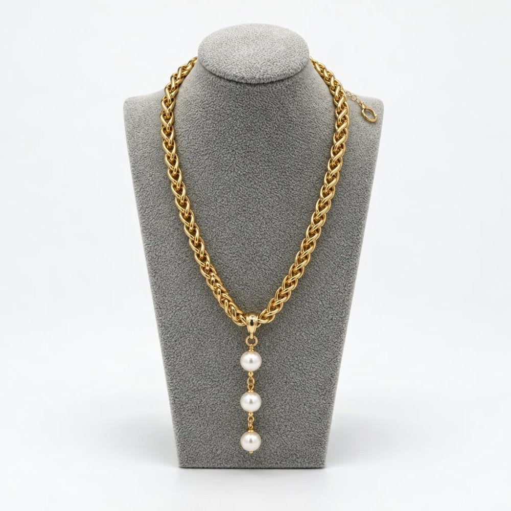 A gold chain necklace with a pendant of three pearls, displayed on a gray stand.