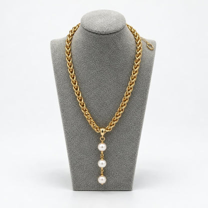 A gold chain necklace with a pendant of three pearls, displayed on a gray stand.
