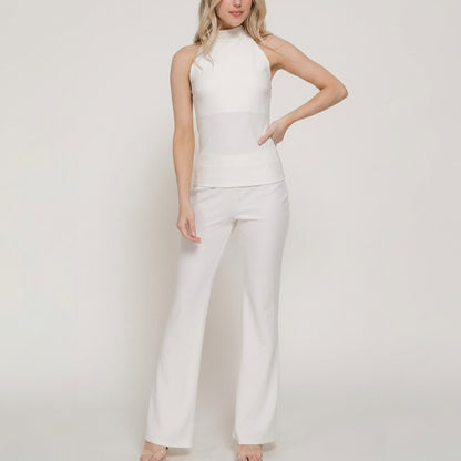 Person in a white sleeveless top and pants, standing against a plain background.