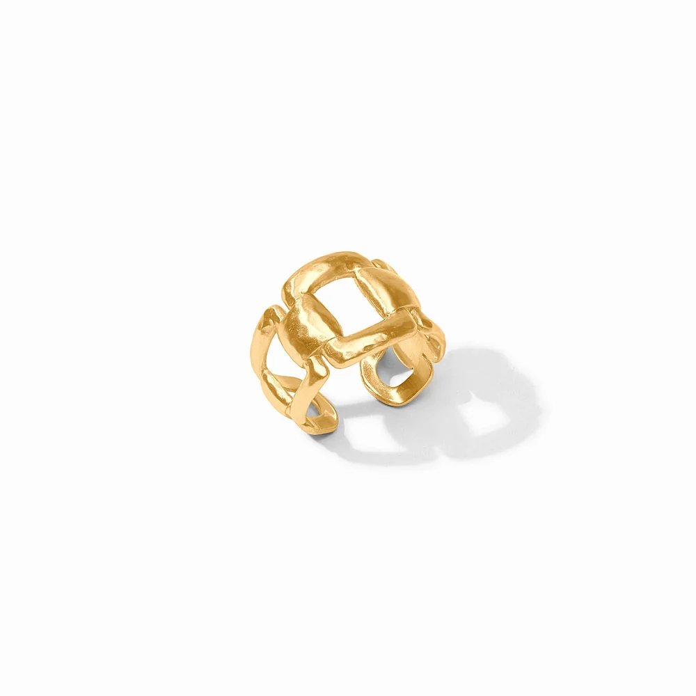 A sculptural gold ring with an interwoven design rests on a white surface.