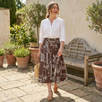 Woman in white top and brown skirt smiling outdoors, holding a straw bag.