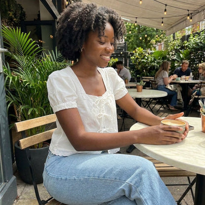 Smiling woman enjoying coffee at an outdoor cafe.
