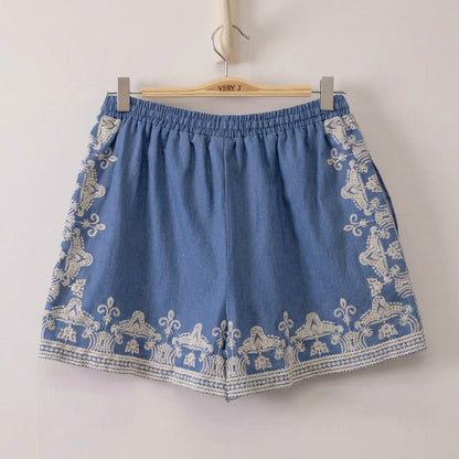 Blue shorts with white intricate embroidery hanging on a hanger.