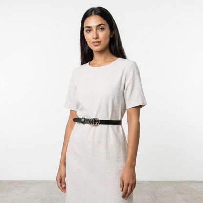 Woman in a beige dress with a black belt against a plain background.