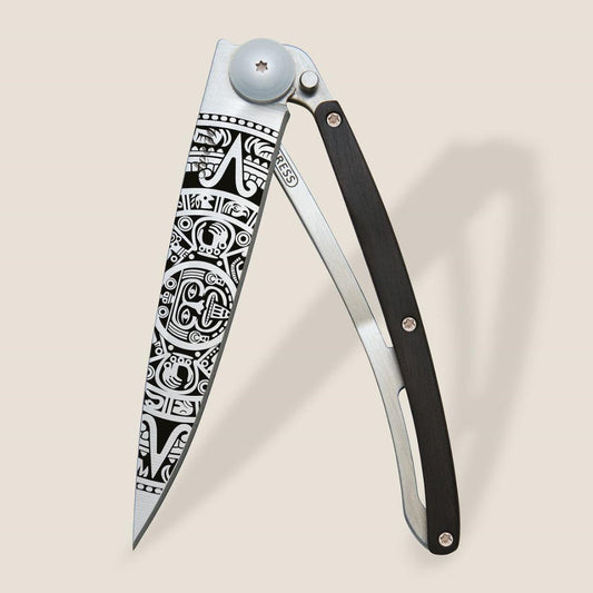 Folding knife with intricate, tribal-style blade design.