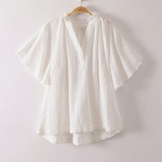 White, flowy blouse with loose sleeves on a hanger.
