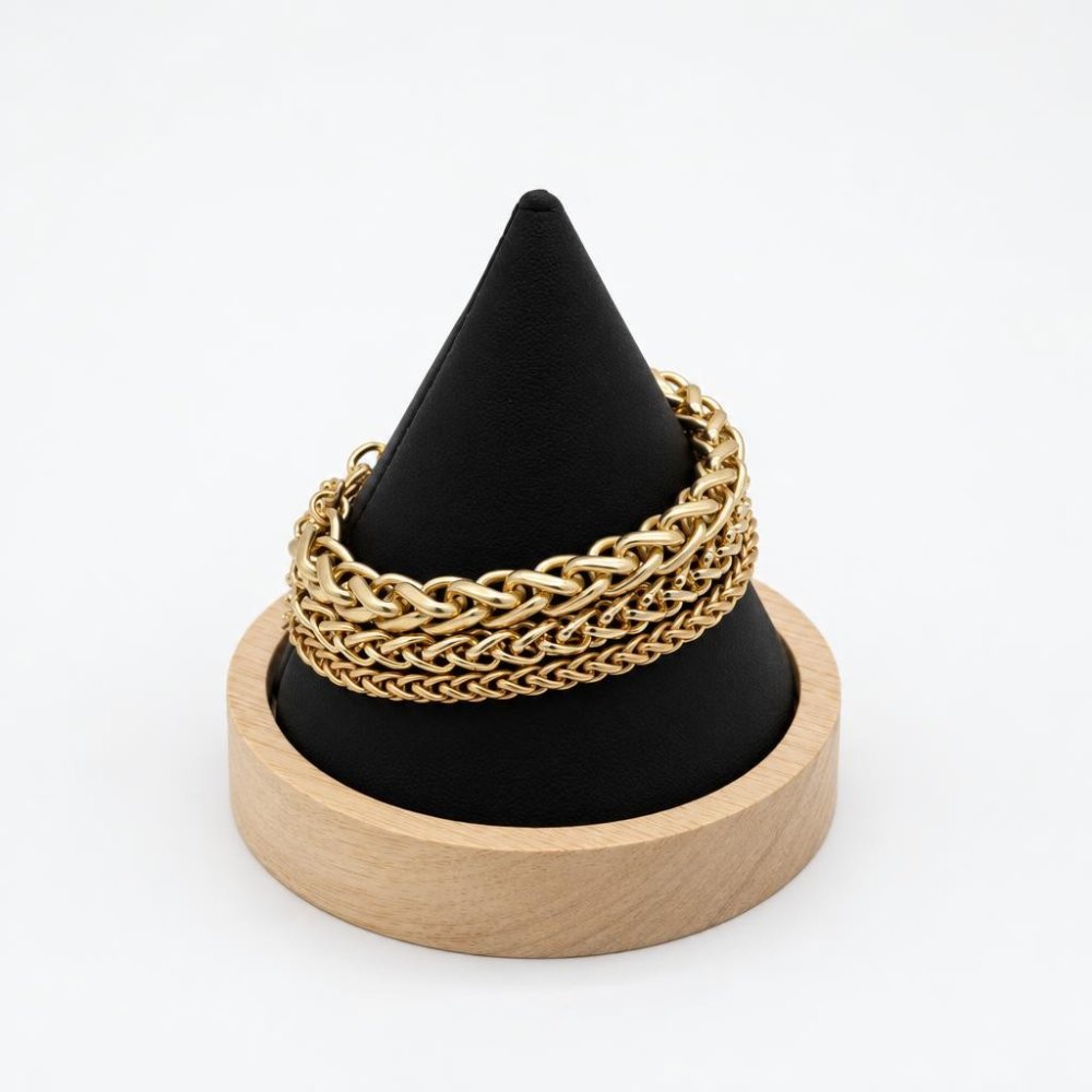 Gold chain bracelets displayed on a black cone-shaped stand with a wooden base.