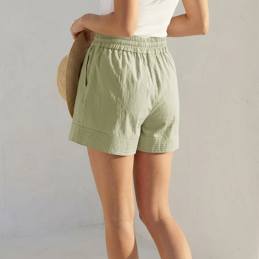 Person in green shorts holding a straw hat.