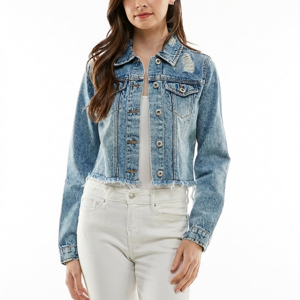 Woman in a denim jacket smiles outdoors with a drink on the table.