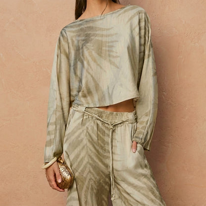Woman in tie-dye outfit holding a small woven bag against a textured wall.
