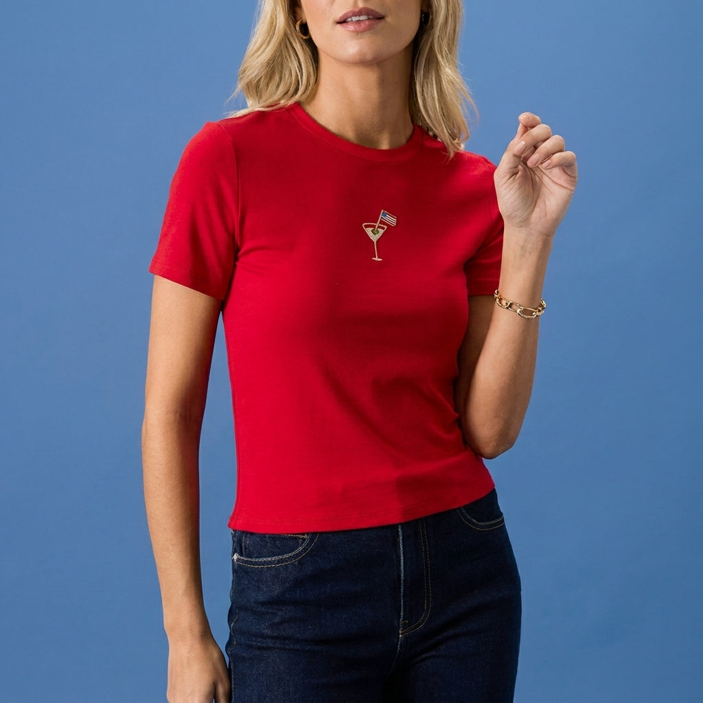 Blonde woman in red shirt with martini graphic, against a blue background.