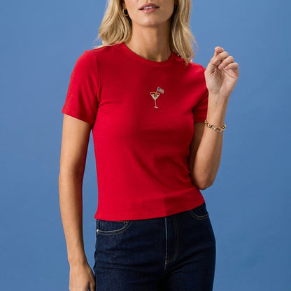 Blonde woman in red shirt with martini graphic, against a blue background.
