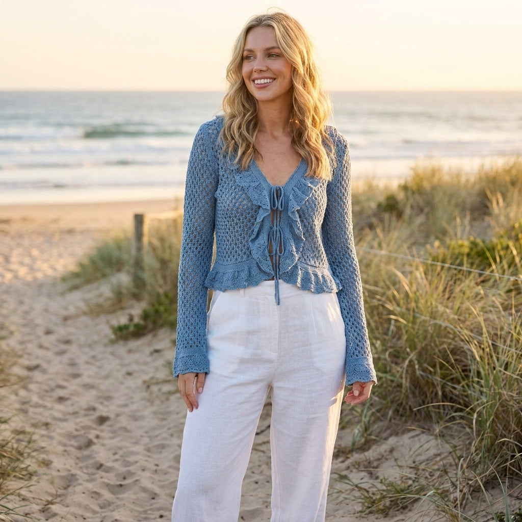 Woman in blue top, white pants on a beach at sunset, smiling.
