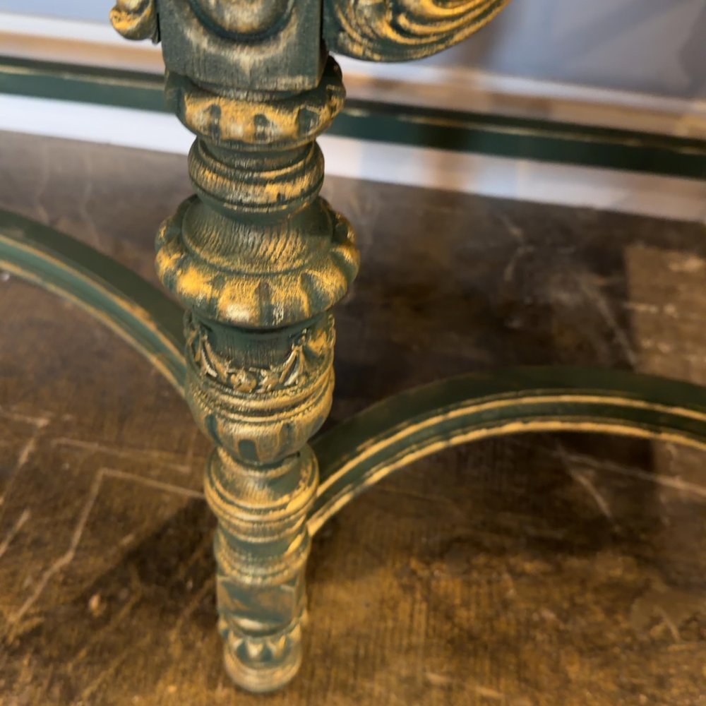 Close-up of an ornate, weathered gold-and-green metal table leg and curved support.
