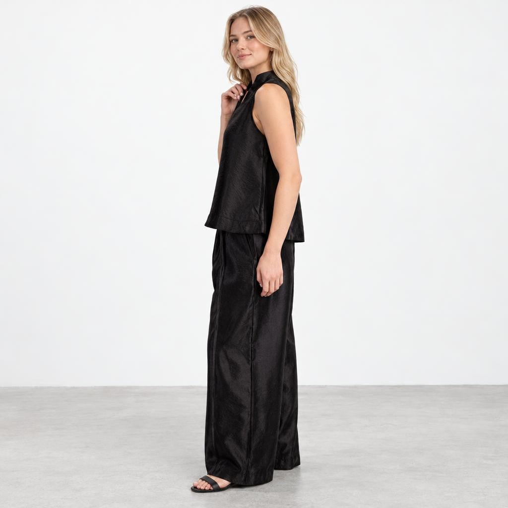 A woman models a black sleeveless top and wide-leg trousers against a plain studio backdrop.