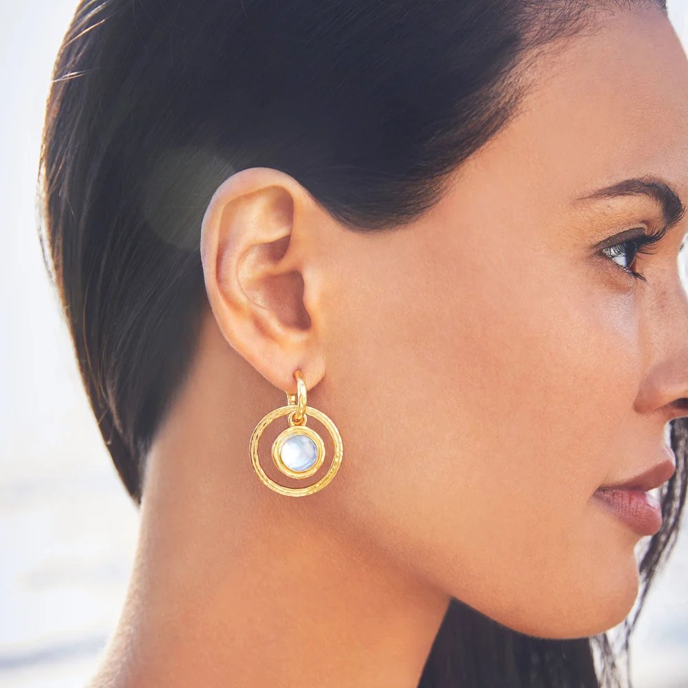 Close-up of a woman wearing a gold circular earring with a pale blue gemstone.