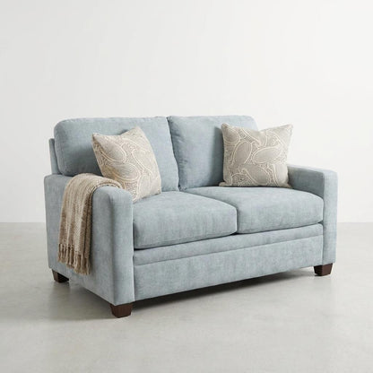 Gray sofa with two decorative pillows on a concrete floor.