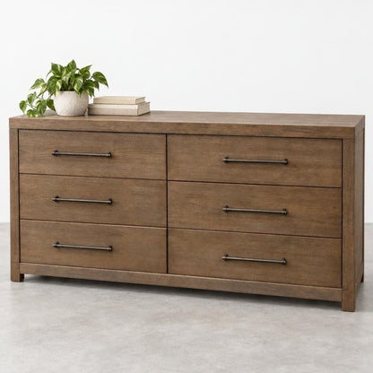 A wooden six-drawer dresser topped with a potted plant and books.