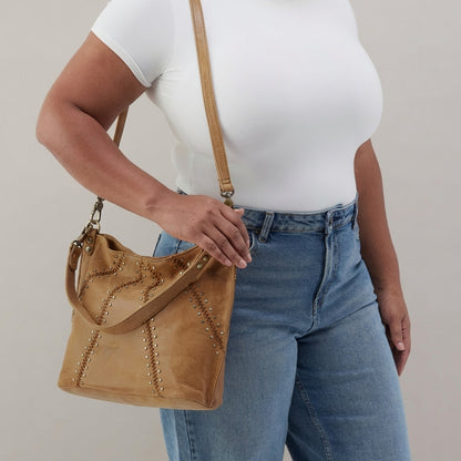 Person with tan bag, white shirt, and jeans poses against neutral background.