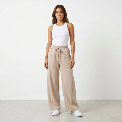 Person in white tank top and beige pants, standing on a gray floor.