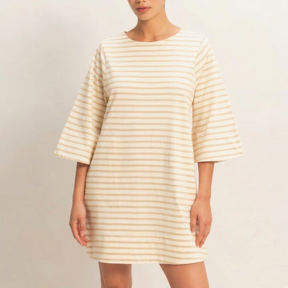 A person in a beige striped, loose-fitting dress with wide sleeves.