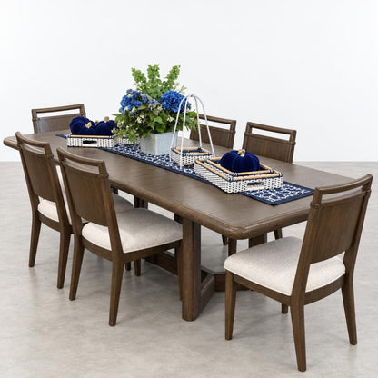 A wooden dining table with upholstered chairs, a blue runner, floral centerpiece, and serving trays.
