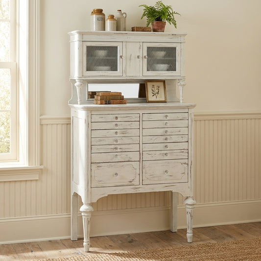 Vintage white cabinet with drawers, glass doors, jars, and plant on top.