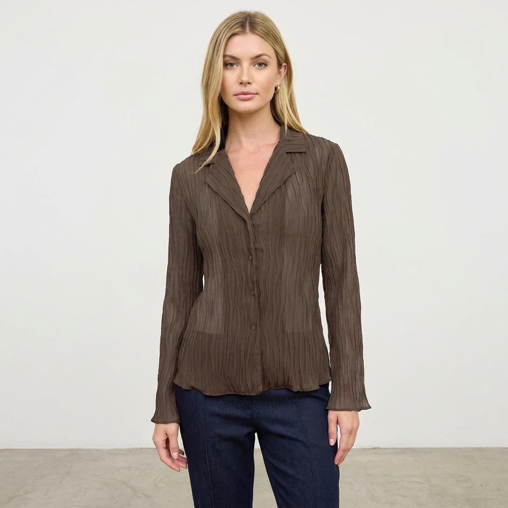 Woman in brown blouse and jeans standing against a plain background.