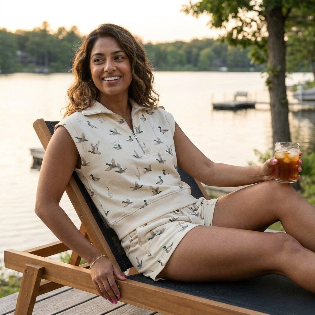 Woman relaxing on a deck chair by a lake, holding a drink, smiling.