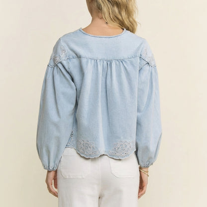 Woman in light blue blouse with floral embroidery, facing away.