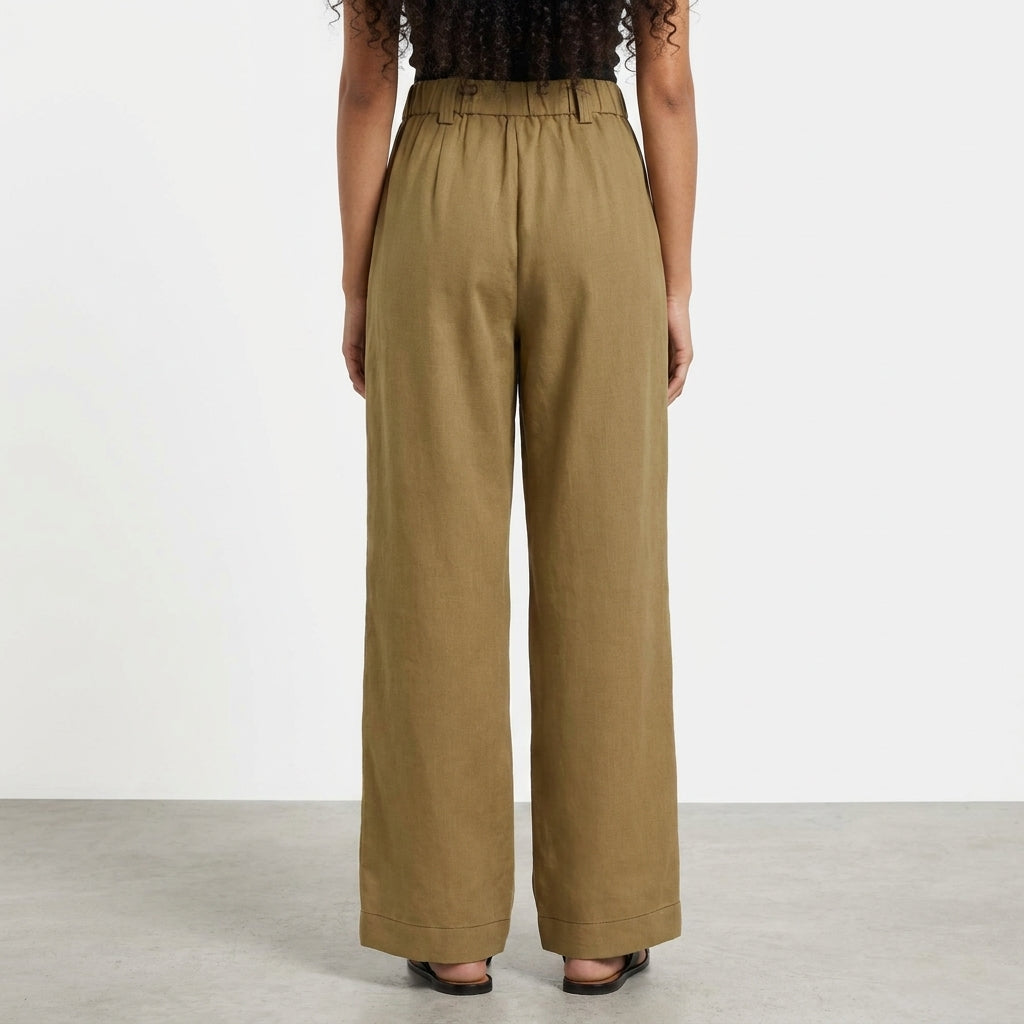 Person in wide-leg brown pants facing away in a minimalist setting.