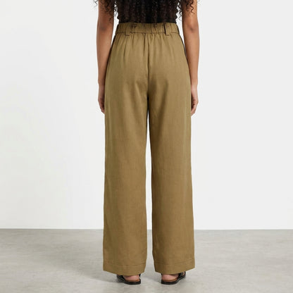 Person in wide-leg brown pants facing away in a minimalist setting.