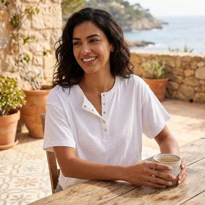 Woman smiling with coffee on a sunny terrace by the sea.