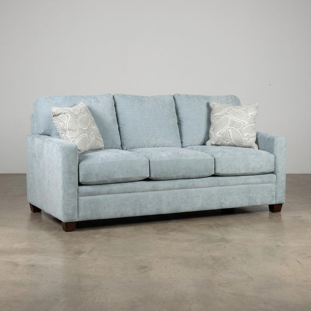 Light blue sofa with paisley pillows on a concrete floor.