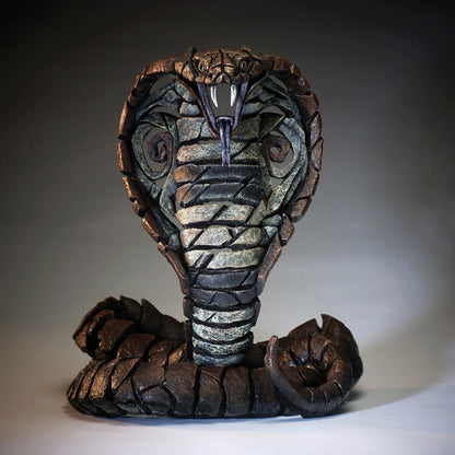 Stone cobra sculpture with fangs bared, on a smooth gray background.